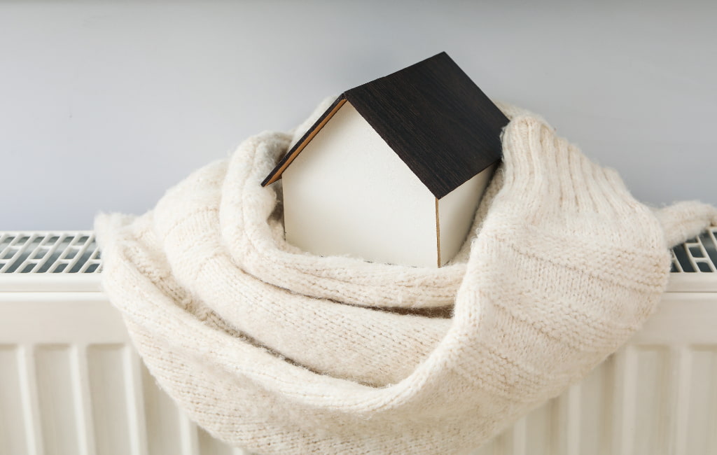 Maison posée sur un chauffage mural, entouré d'une écharpe représentant la chaleur et le confort
